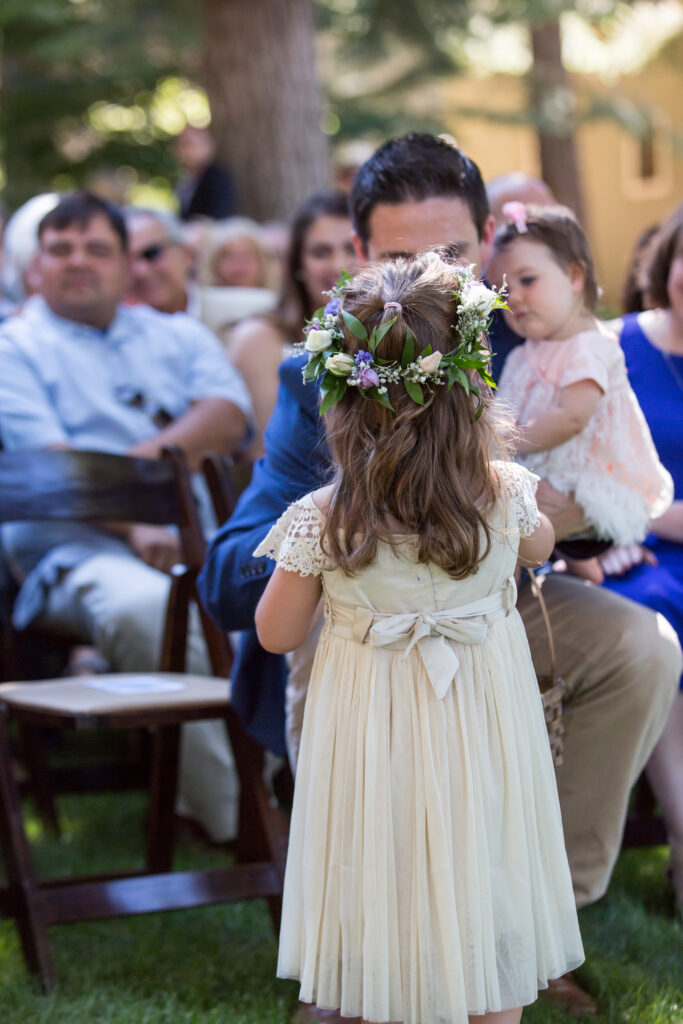 Flower girl with flower crown and bow walks down the aisle and stops to hand out rose petals